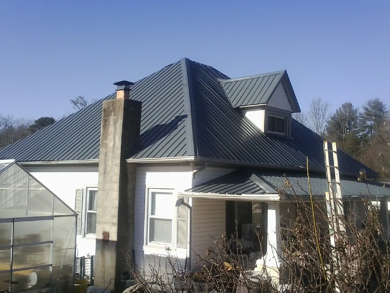 Dark blue standing seam metal roof on a white farmhouse with dormer — Slate & Tile Roof Repair by Roofing Brothers in La Verne