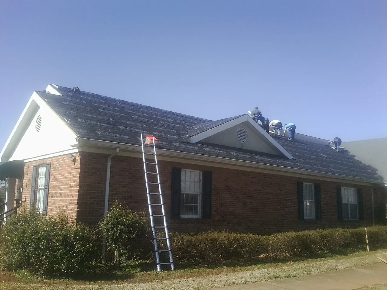 Crew tearing shingles off a brick ranch roof with a ladder set — Metal Roof Repair work by our crew in La Verne