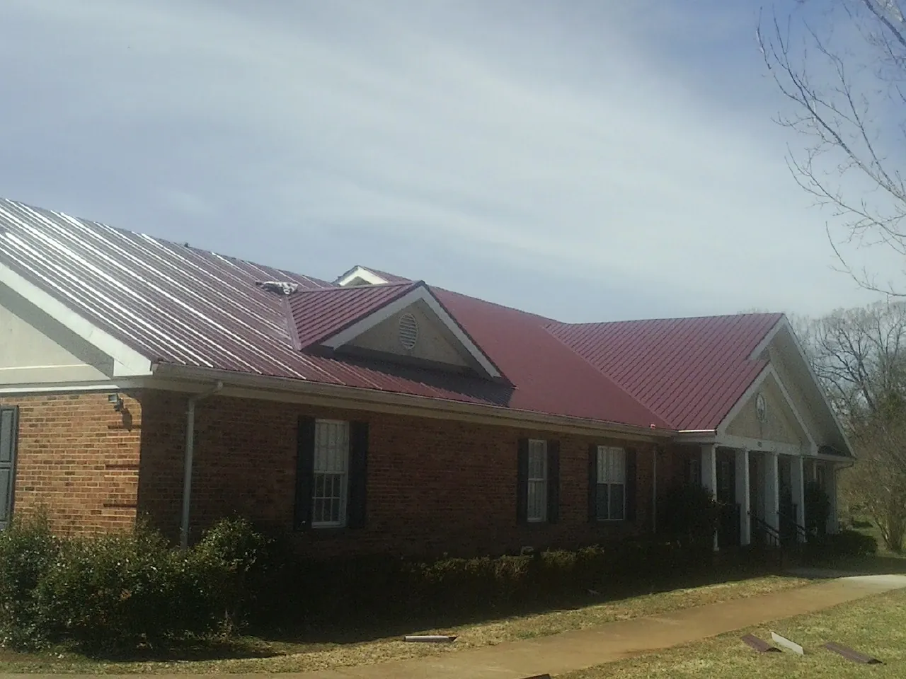 Red metal roof with gabled entries on a long brick building, from a Hail Damage Roof Repair job in La Verne