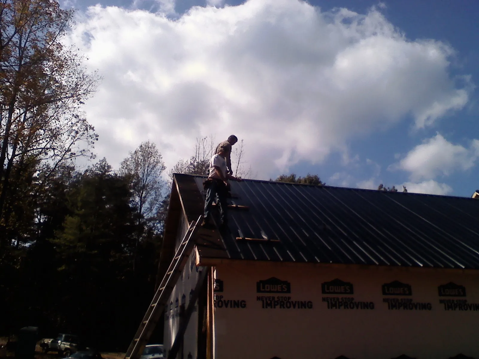 Roofer fastening dark metal panels high against a cloudy sky, from a Roof Inspection job in La Verne