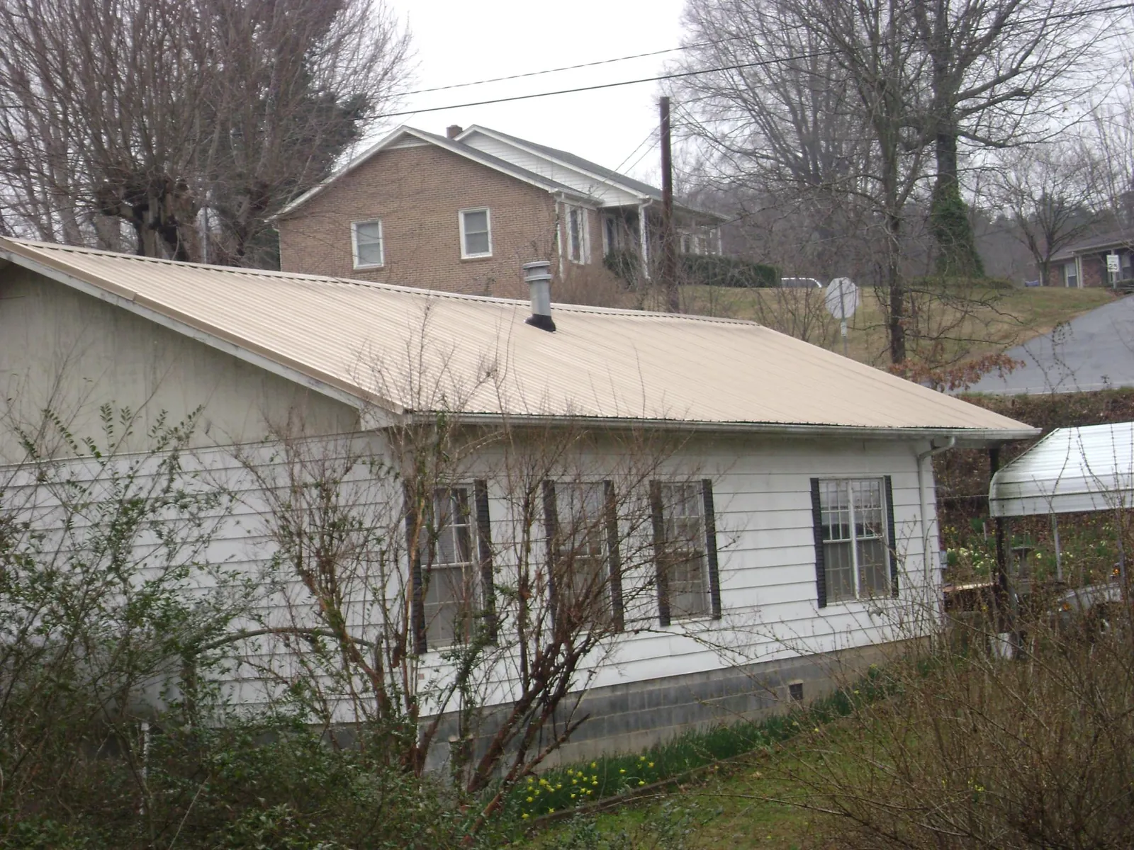 Tan metal roof on a white sided house set into a hillside — Commercial Roofing by Roofing Brothers in La Verne